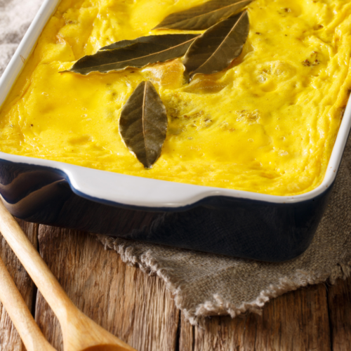 Golden-topped homemade bobotie fresh from the oven in a ceramic baking dish, Cape Malay spiced mince with egg custard topping